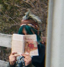 A photo of a person holding a book, their face hidden behind it 