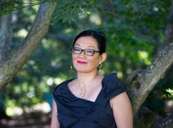 A photo of poet Anna Maria Hong in front of some blurred, bright foliage.