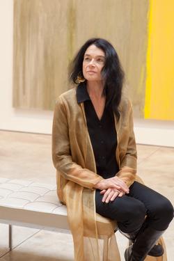 Photograph of Anne Waldman seated on a bench wearing a gold sweater. 