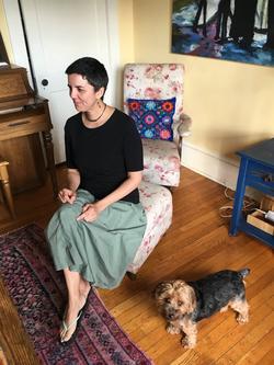 A photo of poet Carmen Giménez Smith sitting in a chair next to a dog.