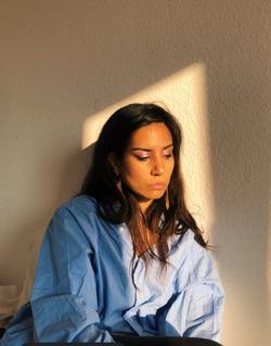 A photo of poet Aria Aber sitting in a patch of sunlight.