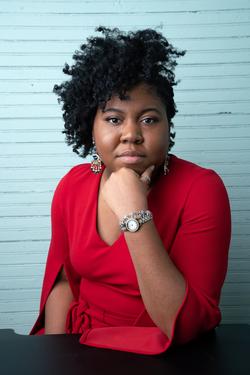 A photo of Ashley Jones wearing red, in front of blue siding.