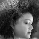 A black and white photo of Yesenia Montilla, with an afro and earrings, eyes closed looking down to the side