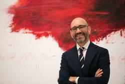 A photo of Carlos Basualdo in front of a painting by Francesco Clemente