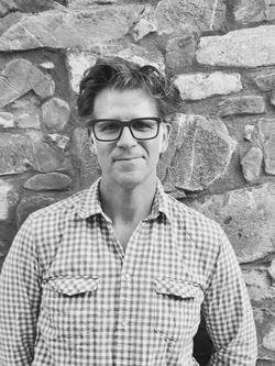 Black and white photo of Curtis Bauer in front of a stone wall