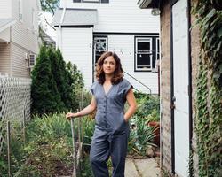 Artist Amy Lincoln stands in a blue jumpsuit in a garden. 