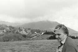 A black and white photo of poet and painter Etel Adnan in a hillside meadow beneath clouds.
