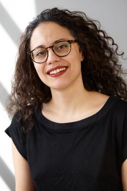 A photo of poet Ghazal Mosadeq wearing glasses and smiling.