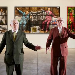 Photo of Gilbert & George in front of one of their artworks.