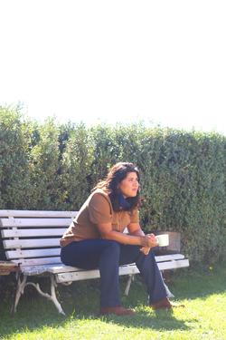 a photo of mónica teresa ortiz sitting on a bench in front of a green tall hedge 