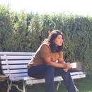 a photo of mónica teresa ortiz sitting on a bench in front of a green tall hedge 