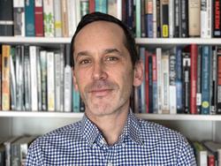 Photo of Judah Schept in front of a bookcase. 