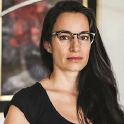 A photo of poet Gabriela Jauregui in front of a red and grey print in a frame.