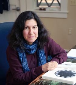 A photograph of poet Jena Osman, sitting at a desk with open books.