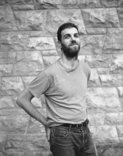 A black and white photo of poet Paul Legault in front of a stone wall.