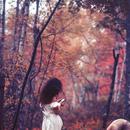 A photo of the back of Manal Kara in a white dress among red trees 