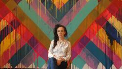 A photo of [Maya Hayuk] in front of one of her colorful murals. 