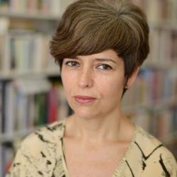 A photo of poet and writer Mónica de la Torre in front of bookshelves.