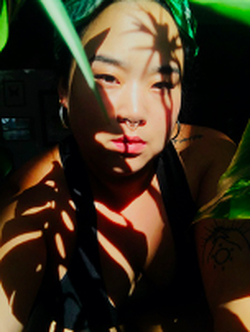 A photograph of poet Mihee Kim in the shadows of leaves.