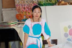 This is a photo of Korean Artist, Minjung Kim at her studio with many colors, including her dress with large, turquoise circles.