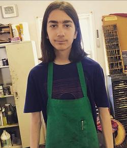 A photograph of poet Patrick Pethybridge wearing a green apron, standing in a printing studio.