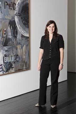 Photo of Michelle White wearing all black standing in front of a painting. 