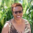 A photograph of poet Patricia Spears Jones, smiling in front of greenery and wearing a floral print.