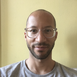 A photograph of Jason Stopa from the shoulders up, wearing glasses and a grey t-shirt