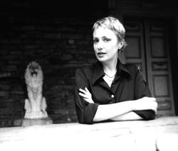 A black and white photograph of poet Sharon Mesmer, with her arms crossed, near a statue of a lion.