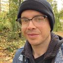 A portrait of Ted Rees in a denim jacket, among fall and green leaves 