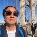 Photo of [Timothy Liu] in sunglasses front of the Brooklyn Bridge. 