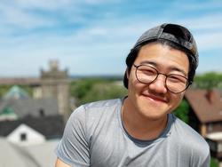 A photograph of poet Yanyi standing in front of blue sky and rooftops.