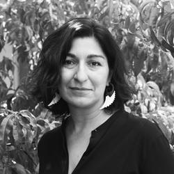 Black and white portrait of writer and curator Yasmeen Siddiqui in front of a green tree. 