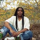 A photo of Yaz Lancaster sitting on the ground in front of a yellow- leafed tree A photo of Yaz Lancaster sitting on the ground in front of a yellow- leafed tree